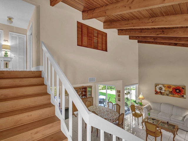 staircase with a towering ceiling, wood ceiling, beamed ceiling, and tile patterned flooring