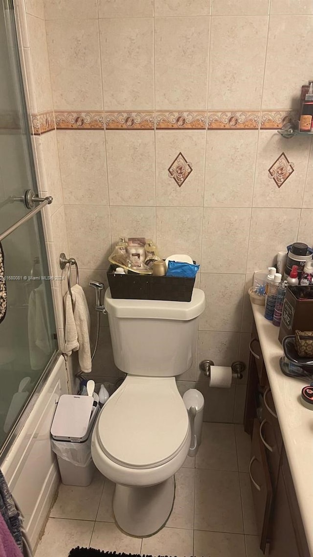 full bathroom with bath / shower combo with glass door, tile walls, toilet, vanity, and tile patterned floors