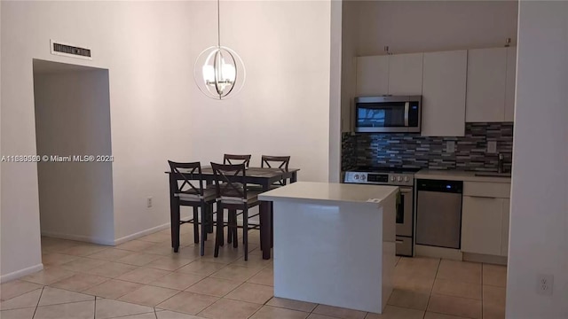 kitchen featuring a kitchen island, backsplash, pendant lighting, white cabinetry, and appliances with stainless steel finishes