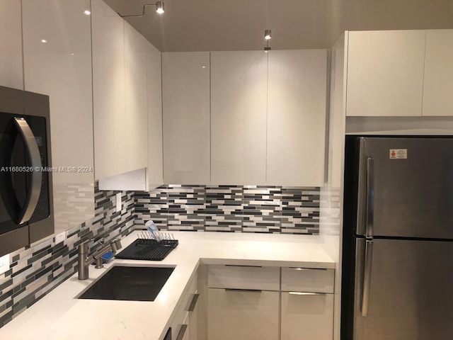 kitchen with tasteful backsplash, appliances with stainless steel finishes, sink, and white cabinets