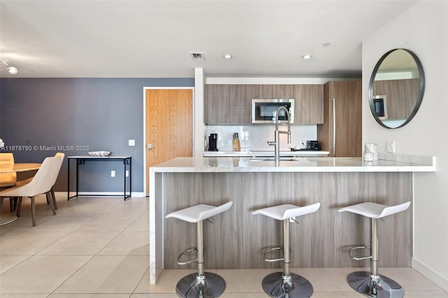 401 N Birch Rd Unit 505, Fort Lauderdale, FL 33304 - kitchen with modern cabinets, a kitchen bar, stainless steel microwave, light tile patterned floors, and a peninsula