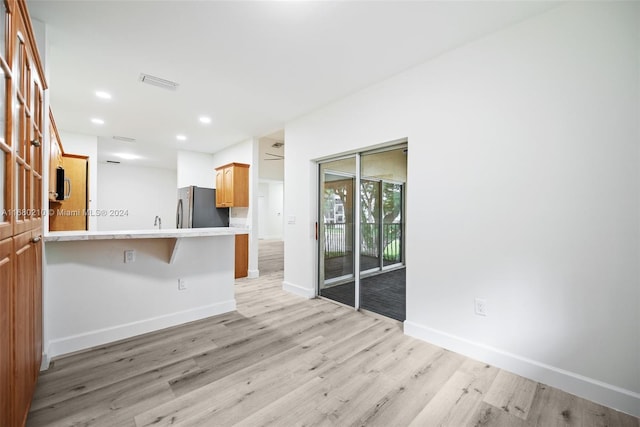 kitchen featuring stainless steel refrigerator, light hardwood / wood-style flooring, kitchen peninsula, and a kitchen breakfast bar