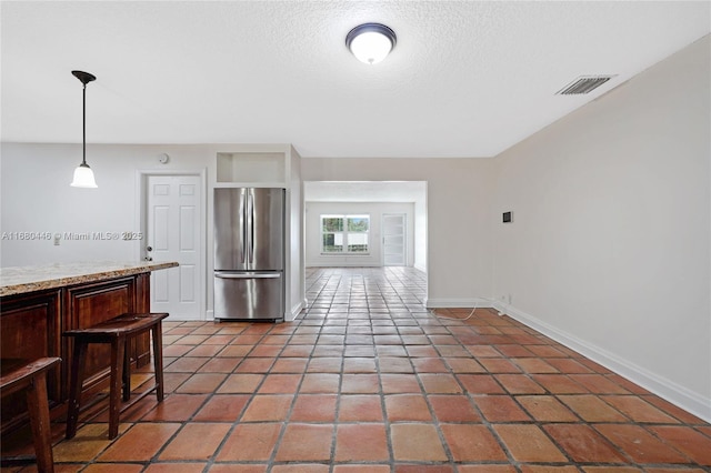 kitchen with a breakfast bar, a textured ceiling, decorative light fixtures, dark brown cabinetry, and stainless steel refrigerator