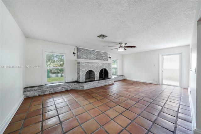 unfurnished living room featuring ceiling fan, a textured ceiling, a wealth of natural light, and a brick fireplace