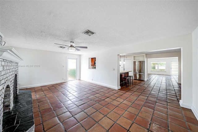 unfurnished living room featuring ceiling fan, a fireplace, dark tile patterned floors, and a textured ceiling