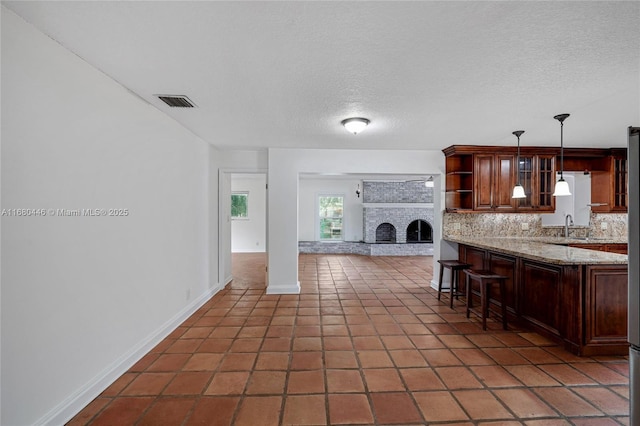 kitchen with pendant lighting, a kitchen breakfast bar, decorative backsplash, dark tile patterned floors, and light stone countertops