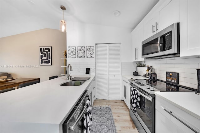 kitchen with white cabinets, appliances with stainless steel finishes, light wood-type flooring, decorative light fixtures, and sink