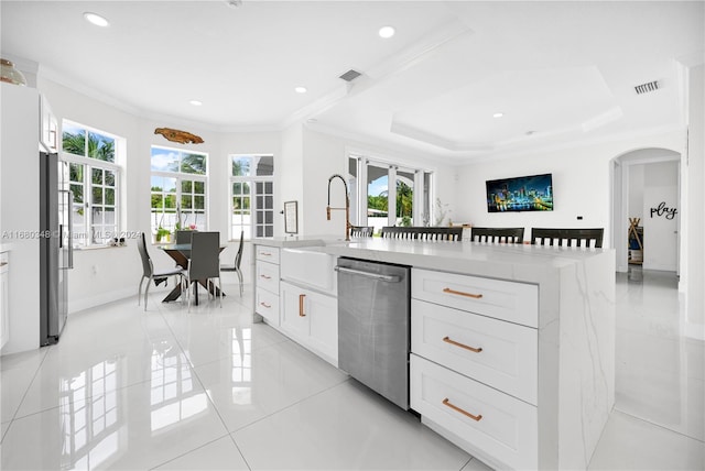 kitchen featuring white cabinets, light tile patterned floors, an island with sink, stainless steel dishwasher, and crown molding