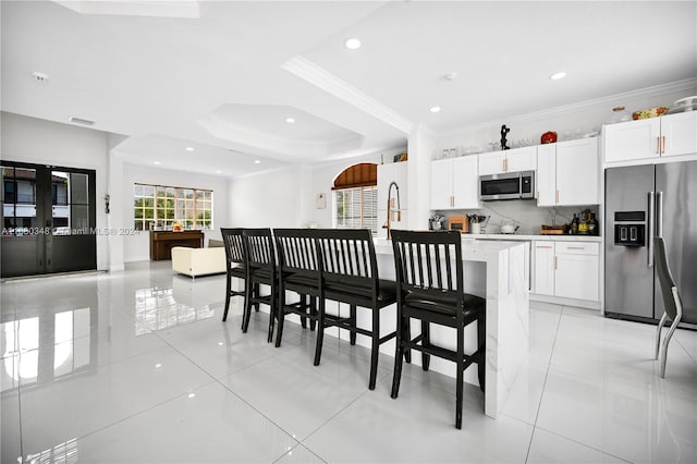 kitchen featuring decorative backsplash, a kitchen island with sink, a tray ceiling, stainless steel appliances, and white cabinetry