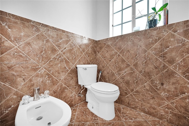 bathroom featuring toilet, sink, a bidet, and tile walls