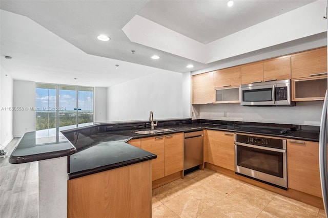 kitchen featuring kitchen peninsula, stainless steel appliances, dark stone countertops, sink, and light hardwood / wood-style floors