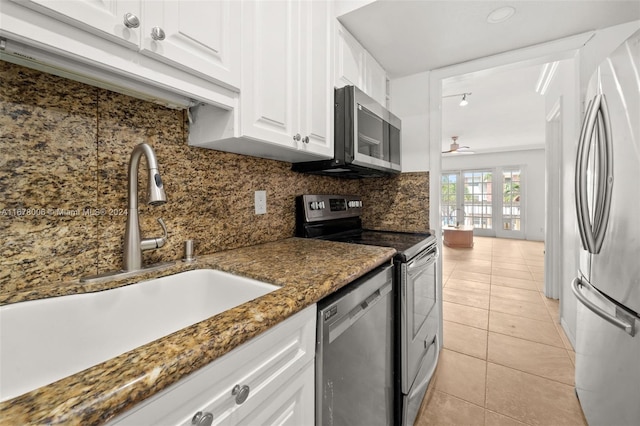 kitchen with stainless steel appliances, dark stone counters, sink, light tile patterned flooring, and white cabinets