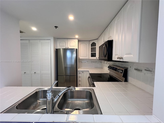 kitchen with decorative backsplash, tile counters, sink, white cabinetry, and appliances with stainless steel finishes