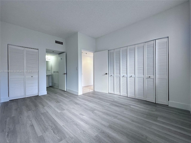 unfurnished bedroom featuring multiple closets, a textured ceiling, hardwood / wood-style flooring, and ensuite bath