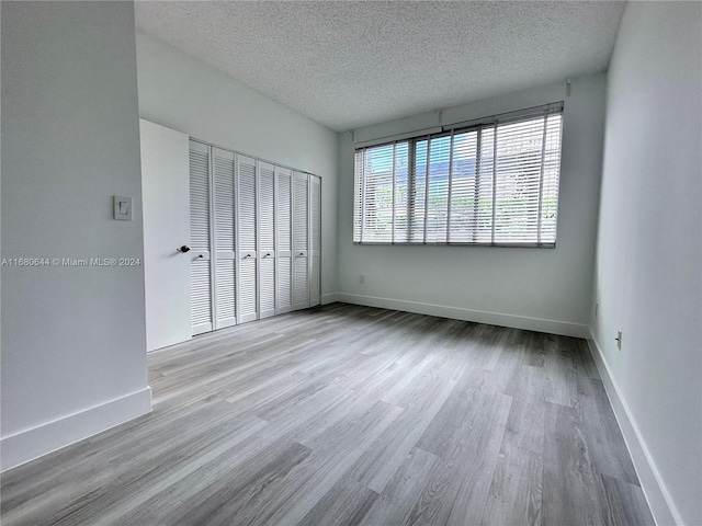 unfurnished bedroom with light hardwood / wood-style flooring, a textured ceiling, and a closet