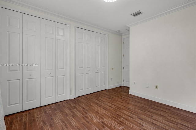 unfurnished bedroom with two closets, crown molding, and dark hardwood / wood-style floors