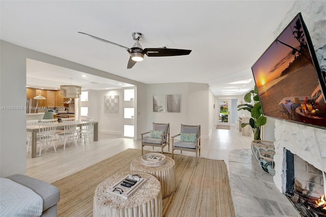 living room featuring ceiling fan, a stone fireplace, and light hardwood / wood-style flooring