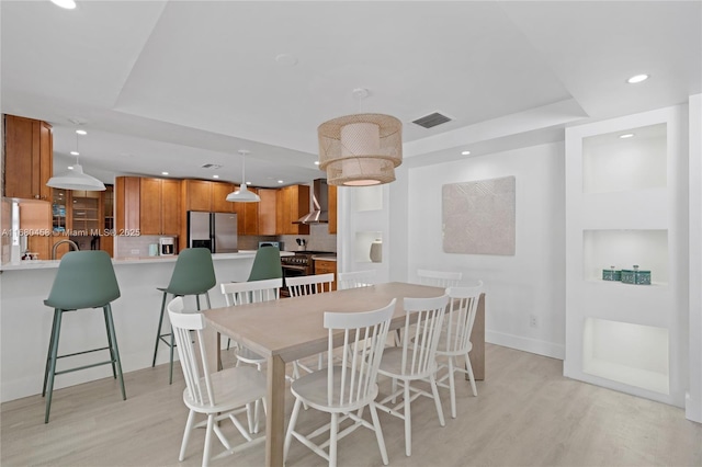 dining room featuring a tray ceiling, sink, and light wood-type flooring