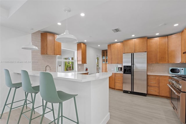 kitchen with kitchen peninsula, appliances with stainless steel finishes, a kitchen bar, light wood-type flooring, and hanging light fixtures