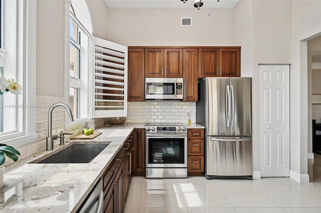 kitchen with light stone countertops, sink, backsplash, stainless steel appliances, and light tile patterned floors