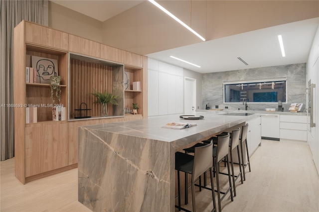 kitchen featuring white cabinets, a kitchen island, white dishwasher, a kitchen bar, and light hardwood / wood-style flooring