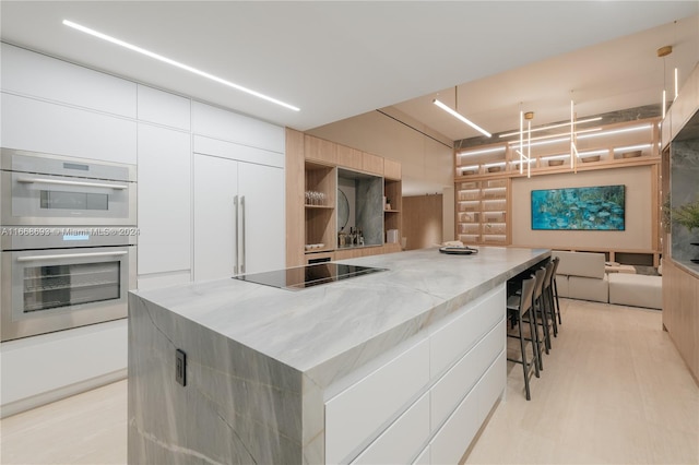 kitchen with a spacious island, black electric stovetop, stainless steel double oven, hanging light fixtures, and white cabinetry