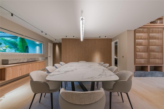 dining room with track lighting, light hardwood / wood-style flooring, and wood walls