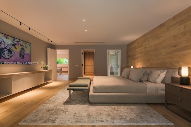 bedroom featuring wood walls, track lighting, and light hardwood / wood-style flooring