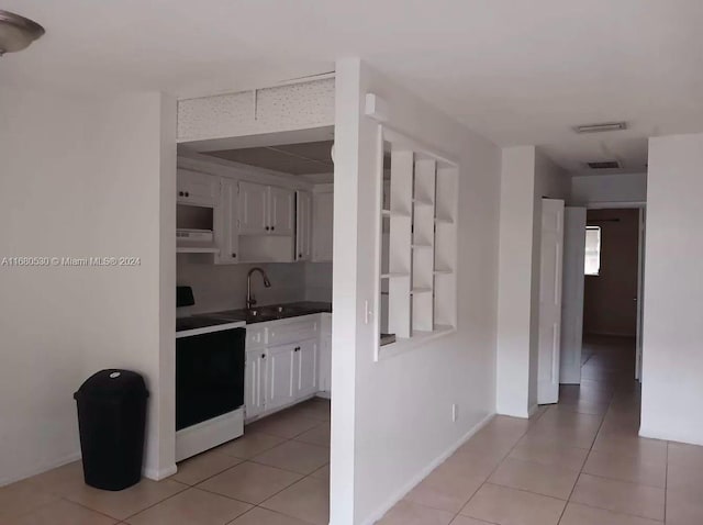 kitchen with light tile patterned flooring, white cabinetry, stove, and sink