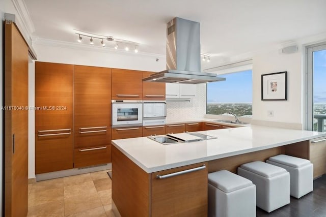 kitchen featuring island exhaust hood, white oven, kitchen peninsula, backsplash, and sink