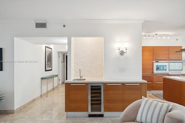 kitchen with oven, ornamental molding, sink, and beverage cooler