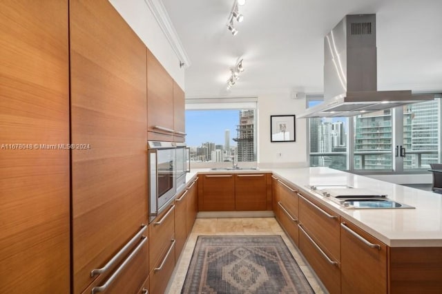 kitchen featuring cooktop, island range hood, stainless steel oven, crown molding, and light tile patterned floors