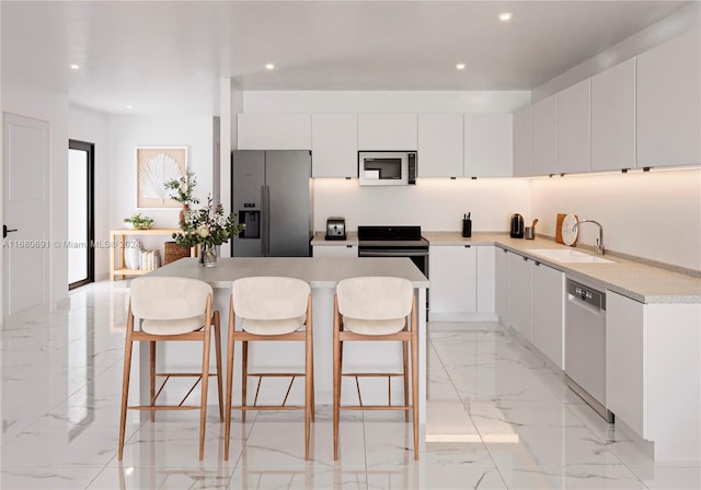 kitchen with appliances with stainless steel finishes, sink, a center island, white cabinets, and a breakfast bar area