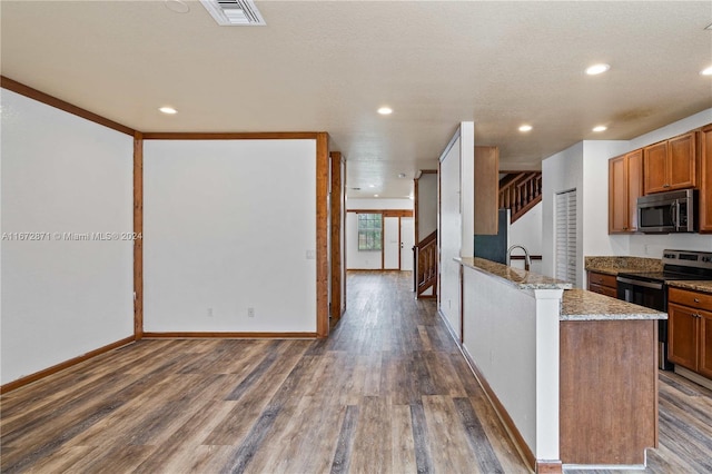 kitchen with appliances with stainless steel finishes, sink, light stone countertops, dark wood-type flooring, and a textured ceiling