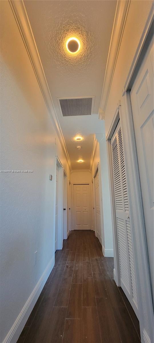 corridor featuring dark wood-type flooring, a textured ceiling, and ornamental molding