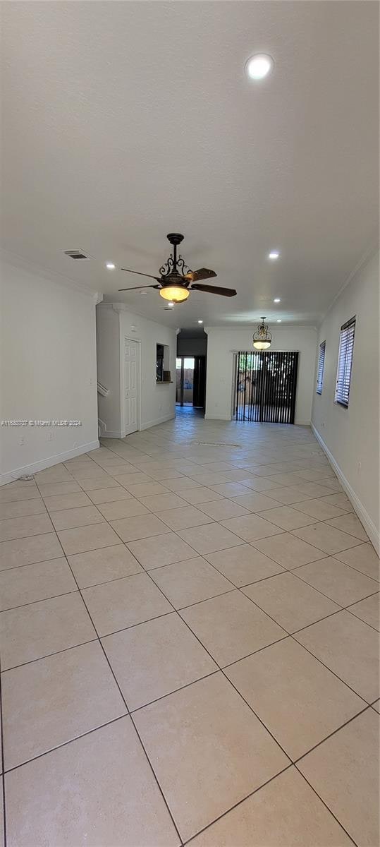 unfurnished living room featuring ceiling fan, crown molding, and light tile patterned floors