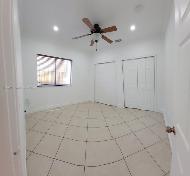 unfurnished bedroom featuring multiple closets, ceiling fan, and light tile patterned floors