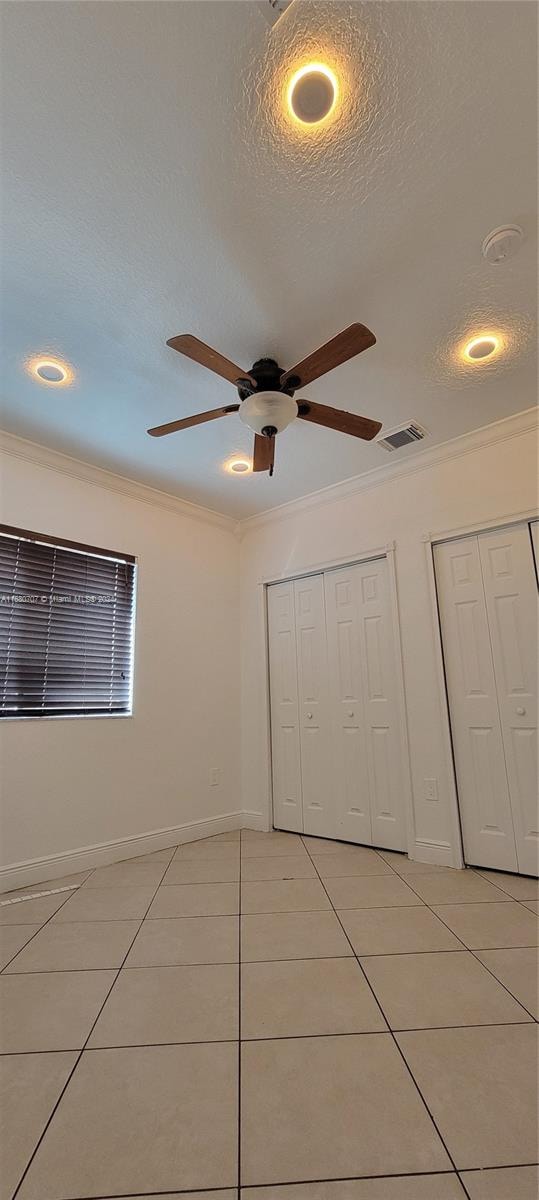 unfurnished bedroom featuring ceiling fan, crown molding, a textured ceiling, light tile patterned flooring, and two closets