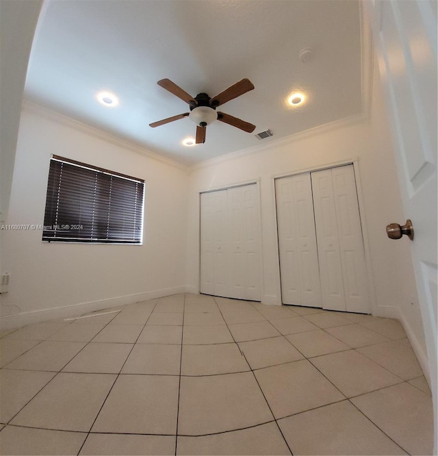 unfurnished bedroom with light tile patterned floors, crown molding, ceiling fan, and multiple closets