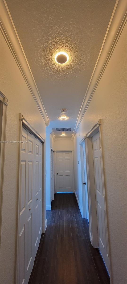 hall featuring a textured ceiling, dark hardwood / wood-style floors, and crown molding