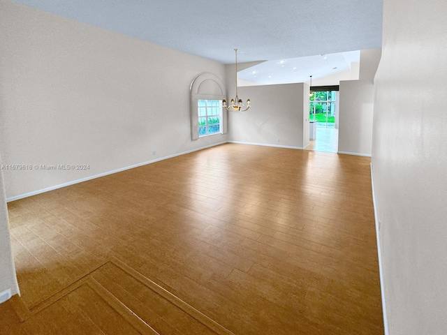 spare room with a wealth of natural light, lofted ceiling, hardwood / wood-style floors, and an inviting chandelier