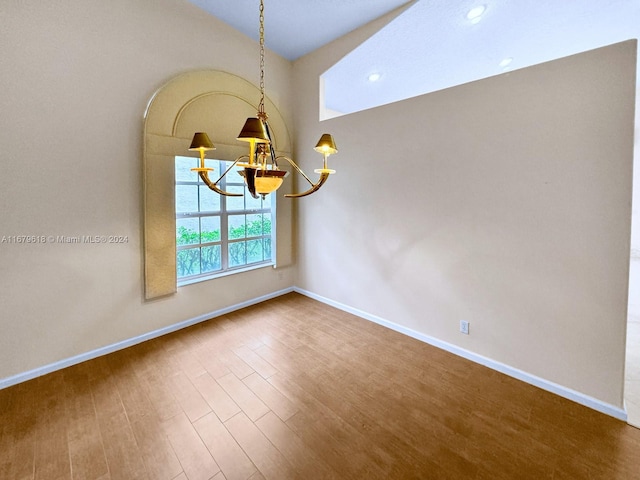 spare room featuring wood-type flooring and a chandelier