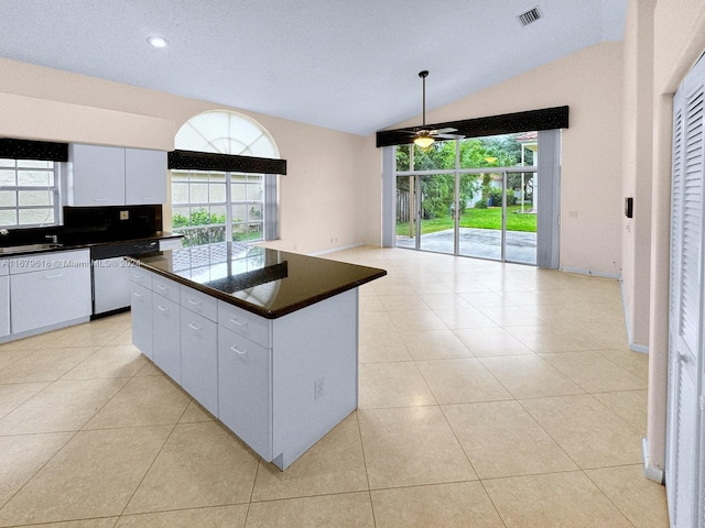 kitchen with lofted ceiling, dishwashing machine, a center island, light tile patterned flooring, and white cabinets