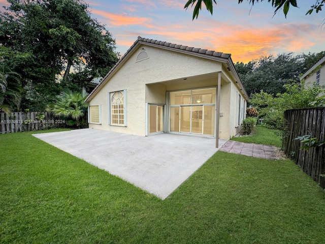 back house at dusk featuring a patio area and a lawn