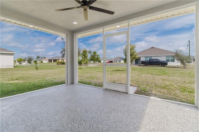 unfurnished sunroom featuring a ceiling fan and a residential view