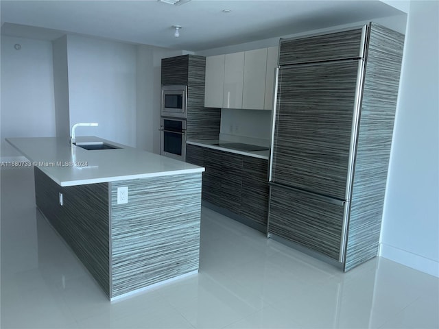 kitchen featuring white cabinets, light tile patterned floors, appliances with stainless steel finishes, a kitchen island with sink, and sink