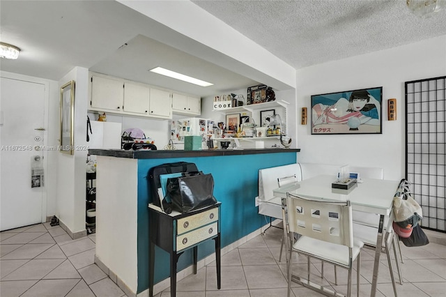 kitchen featuring kitchen peninsula, a textured ceiling, white cabinetry, and light tile patterned flooring