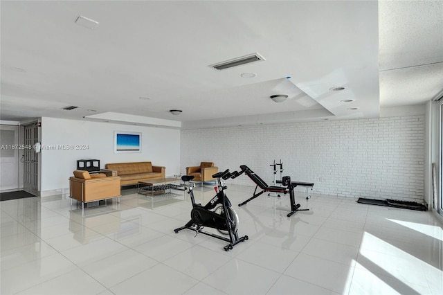 exercise room with light tile patterned floors and brick wall