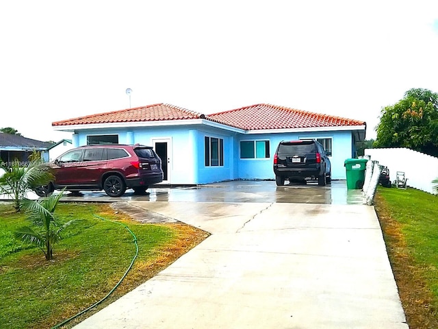 mediterranean / spanish home with a tile roof, driveway, a front lawn, and stucco siding