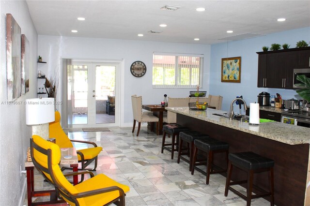 kitchen with stainless steel appliances, light stone countertops, a kitchen bar, and french doors